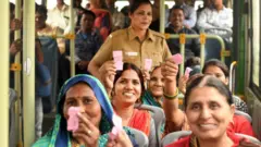 बसों में अपने गुलाबी टिकट दिखाती महिलाएं