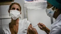 Enfermeira aplica vacina em mulher, ambas de máscara