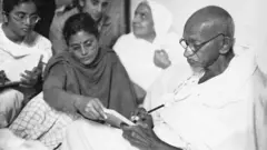 Gandhi escribiendo mensaje con ayuda de Abha y Manu, tras interrumpir su ayuno, Nueva Delhi, India, 1948.