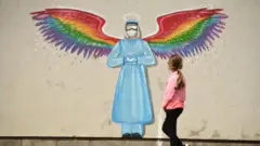 A girl walks past a mural of a doctor with rainbow angel wings