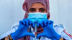 صورة محجبة مع عينة من شخص وتقوم بعمل إشارة "قلب" بأصابعها