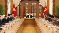 En esta imagen divulgada por los medios estatales de Corea del Norte se va a un numeroso grupo de funcionarios usando mascarillas mientras asisten a una reunión con Kim Jong-un sobre la estrategia contra el covid-19.