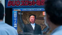 People in Tokyo walk past a TV screen showing Kim Jong-un