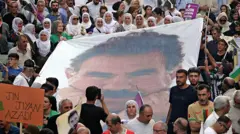 Öcalan'ın posterini taşıyan çoğu geleneksel giysili kadınlardan oluşan bir grup. Sol altta Jin, Jiyan, Azadi yazılı bir pankart tutan bir başka kadın görünüyor. Eylül 2025