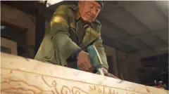 Seorang pembuat peti mati mengukir kayu.