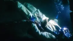Mergulhador caído no fundo do mar em cena de documentário