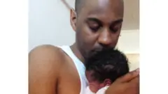 Elliott segura bebê recém-nascida no colo