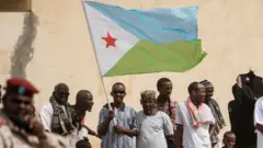 People hold Djiboutian national flag as they wait for the arrival of Djibouti's President Ismail Omar Guellehas before the launching ceremony of new 1000-unit housing contruction project in Djibouti, on July 4, 2018.