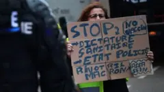 Un manifestant tient une pancarte anti-vaccins devant des gendarmes.