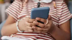 دو دست یک فرد که سر او در عکس نیست، یک موبایل را گرفته