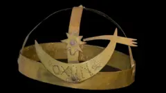 Une coiffe en forme de couronne sur laquelle est gravé le mot Oxun.