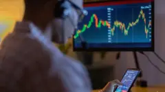 رجل يتابع عملات رقمية على حاسوب وهاتف