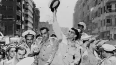 الجنرال نجيب يرفع قبعته العسكرية وخلف البكباشي عبد الناصر