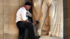 ሃውልቱን በመዶሻ እየመታ ያለ ግለሰብ