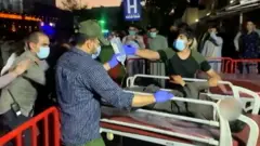 pessoas com máscara empurram maca com pessoa em cima