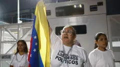 Uma mulher segurando a bandeira da Venezuela e usando uma blusa escrito "Liberta todos os presos políticos"