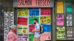 Dos personas caminan frente a un supermercado en Caracas.