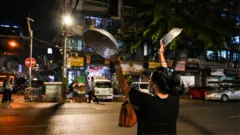 A woman clatters pans to make noise after calls for protest went out on social media in Yangon