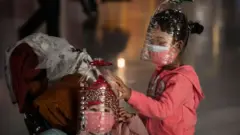 Chinese children wear plastic bottles as makeshift homemade protection and protective masks while waiting to check in to a flight at Beijing Capital Airport on January 30, 2020 in Beijing, China.