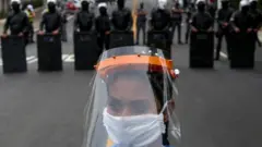 Woman in mask and face shield in front of police