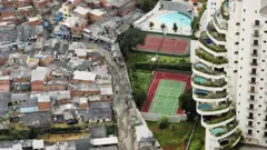 Foto mostra favela ao lado de condomínio de luxo, com piscinas nas varandas