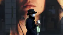 A woman wearing a protective mask walks past a store window in the city of Munich