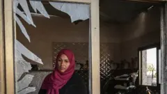 فلسطينية تنظر من خلال نافذتها المهشمة في خان يونس