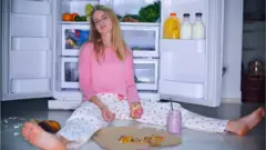 Chica comiendo al lado de la nevera en piyama