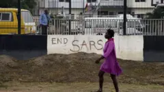 A pedestrian walks past a road divider adorned with EndSars graffiti
