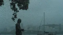 Atrás de janela molhada por pingos de chuva, homem é visto em pé em calçada na orla do Rio de Janeiro