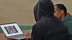 Um moderador, visto de trás e com um capuz escuro para mantê-lo anônimo, mostra ao repórter da BBC um laptop com imagens desfocadas do TikTok