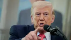 O presidente dos EUA, Donald Trump, vestindo terno e gravata vermelha, aponta com um dedo enquanto fala ao microfone.