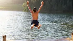 Young boy jumping into lake