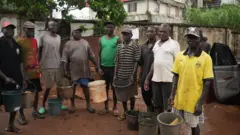 Group of men wey dey hold bucket