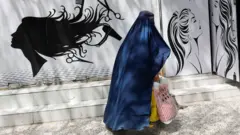 An Afghan woman walks past a beauty salon in Kabul, Afghanistan. Photo: 6 July 2023