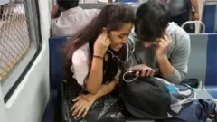 செல்பேசியில் பாடல் கேட்கும் ஆணும், பெண்ணும்