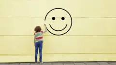 Menina de costas desenha rosto feliz na parede