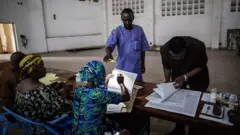 Un électeur congolais utilise son téléphone portable pour éclairer le personnel électoral lors de l'ouverture du bureau de vote pour les élections présidentielles à Brazzaville le 20 mars 2016.