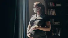 Picture of pregnant lady with mask looking out of window