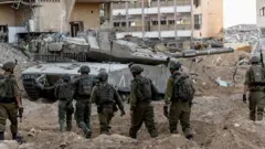Israeli soldiers walking through the rubble in the northern Gaza Strip next to an army tank