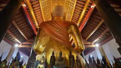 Enorme estátua dourada de Buda, de costas, com diversas outras menores, de frente