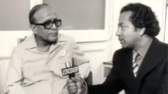 ভারতের পশ্চিমবঙ্গ রাজ্যের তৎকালীন মুখ্যমন্ত্রীর সাক্ষাৎকার নিচ্ছেন শ্যামল লোধ। সাথে আছেন বাংলা বিভাগের তৎকালীন প্রধান জন রেনার।