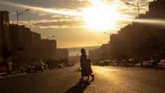 በጋራ መኖሪያ ቤቶች መሃል የሚያልፍ አስፋል ላይ እናትና ልጅ ሲሻገሩ።