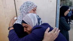 Women hug each other during the funeral of Palestinians killed in Israeli strikes, at al-Awda Hospital, in central Gaza (20 October 2025)