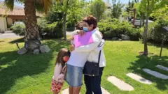 Camila, criança e Aurea se abraçam