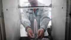 Un empleado del fabricante japonés de condones Sagami Rubber Industries pone un condón en una máquina para probar su resistencia llenándolo de aire.