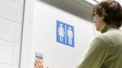 Uma pessoa com a mão na porta de um banheiro cuja placa indica que é unissex