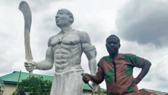 Monday Aigbe aux côtés d'une statue de son arrière-grand-père
