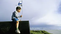 Niño con bandera de Finlandia sentado en un cañon