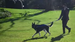 Major is walked by a staff member in the White House grounds on 29 March 2021